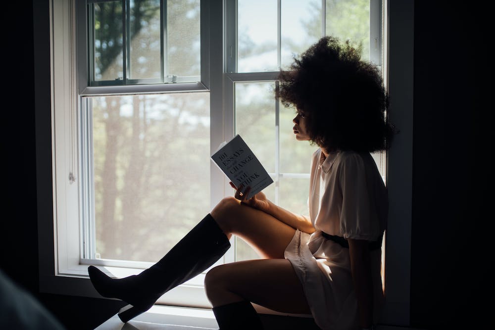 Black woman reading a book in window